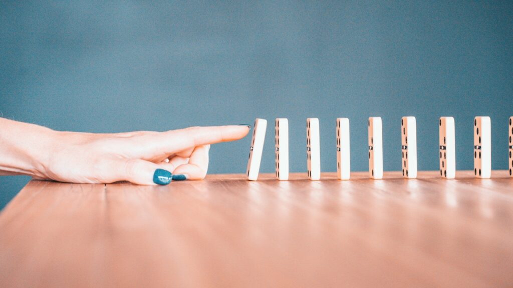 A finger pushing over a row of white dominos